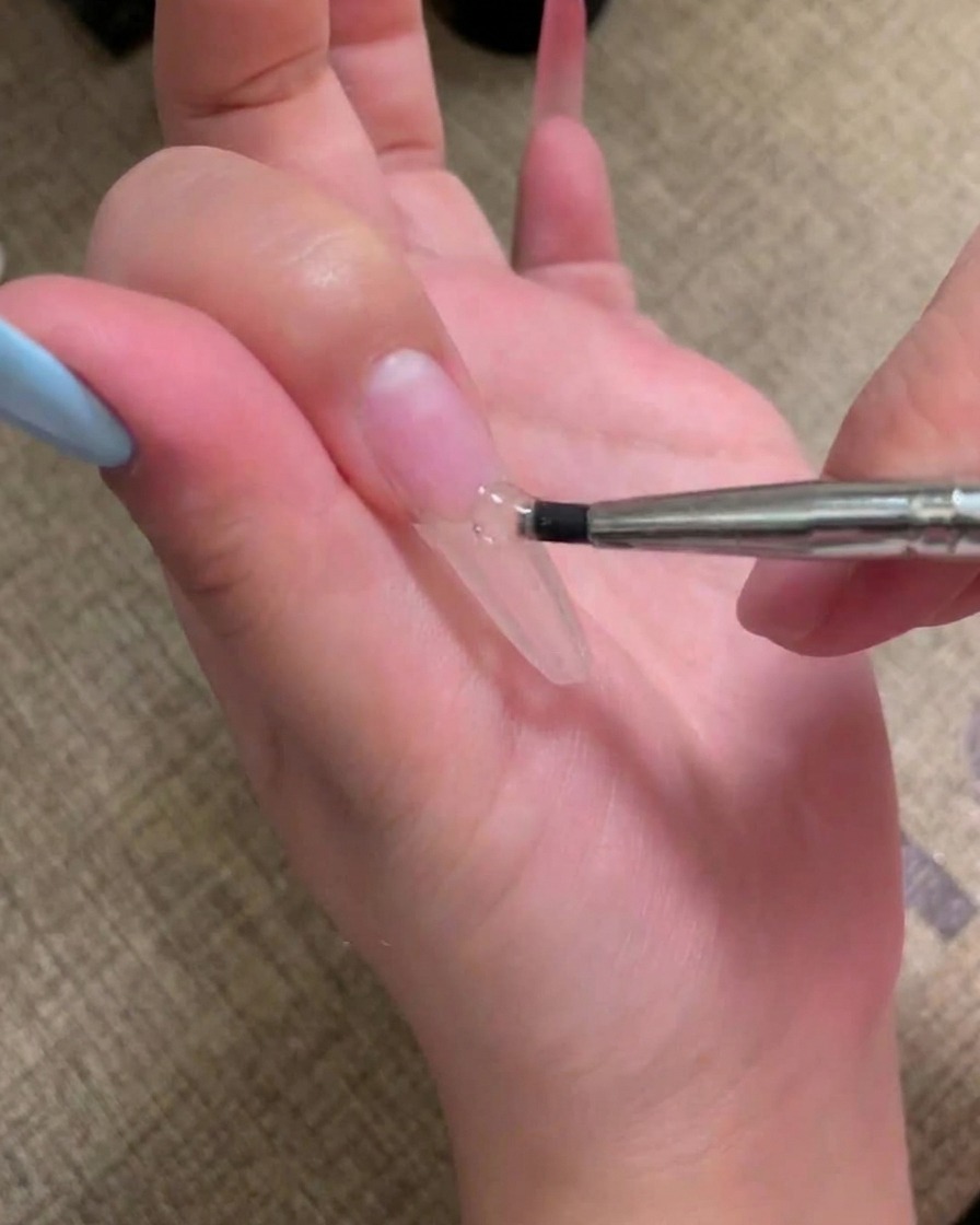 Un pennello applica uno strato di smalto gel rosa carne su ununghia preparata.