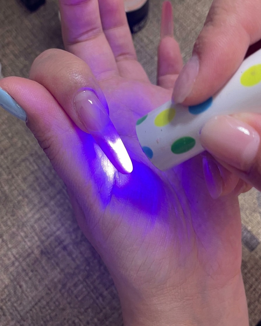 Una mano tiene una lampada UV portatile direttamente sopra le unghie per polimerizzare lultimo strato di gel.