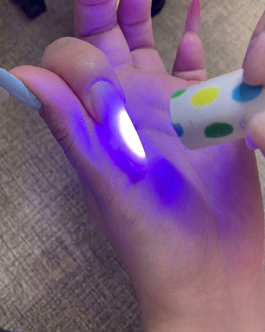 Una mano polimerizza lunghia con punta sfumata sotto una lampada UV, con la luce che illumina lunghia.