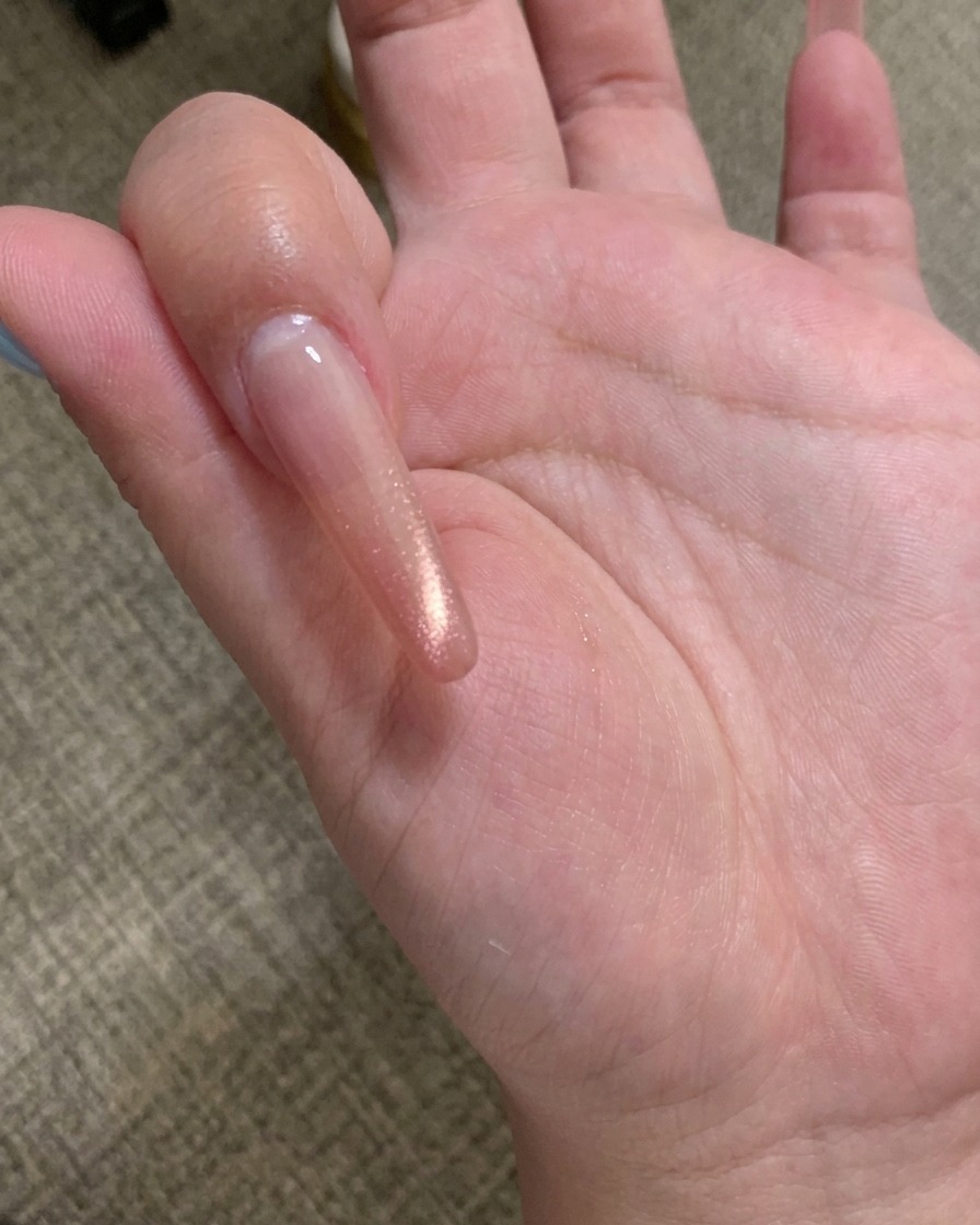 Un primo piano di uno strumento magnetico per unghie tenuto sopra ununghia rivestita di gel cat eye champagne, mostrando le particelle che si allineano.