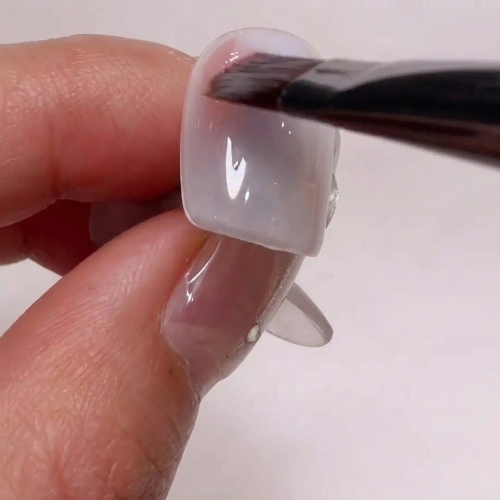 Un pennello da nail art che applica un gel rosa nude sugli angoli laterali di una tip.