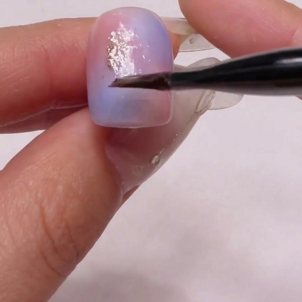 Un pennello che posiziona con cura particelle di glitter dorato sulla superficie dellunghia.