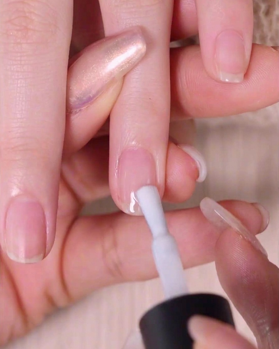 Primo piano di una mano che applica uno smalto bianco semitrasparente su ununghia.
