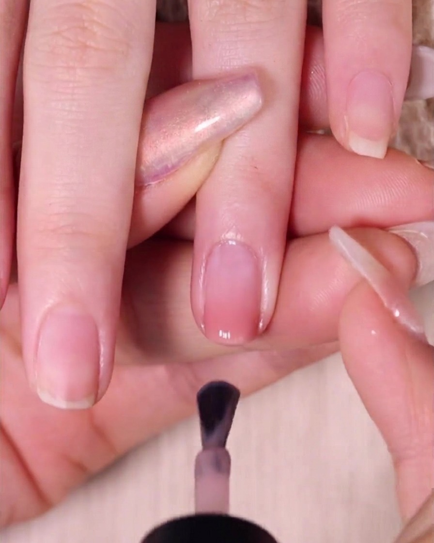 Un pennello applica un leggero strato di smalto nude pink sullunghia, lasciando uno spazio vicino alla cuticola.