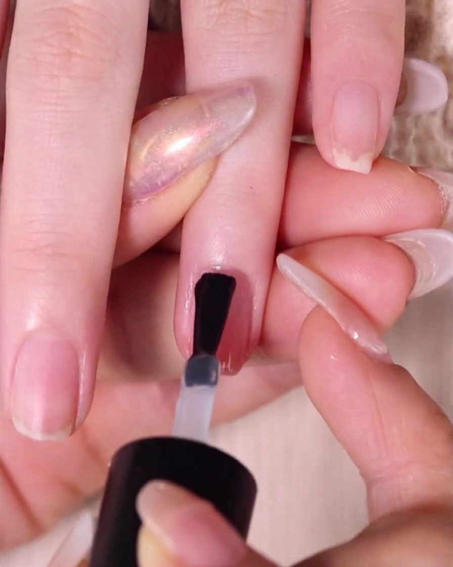 Un pennello che applica uno strato lucido di top coat su ununghia ombré finita.