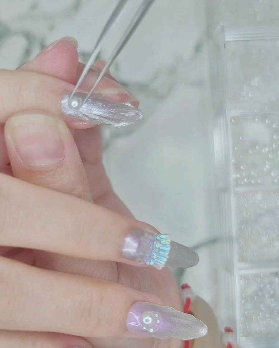 Una pinzetta che posiziona piccole perle bianche sulla linea di gel trasparente umido sullunghia.