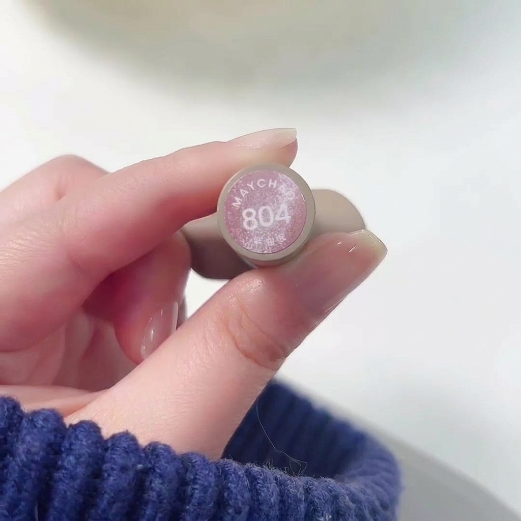 Mano che tiene il flacone di Meichao 804 Taozhi Yaoyao mentre applica lo smalto rosa nude shimmer su ununghia.