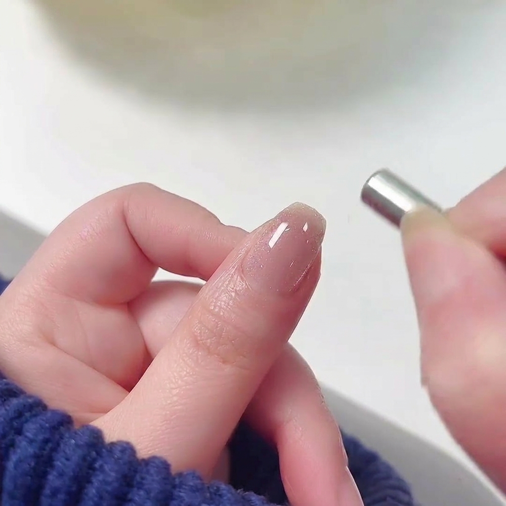 Un piccolo magnete cilindrico tenuto vicino alla cuticola di ununghia con smalto gel cat-eye rosa bagnato.