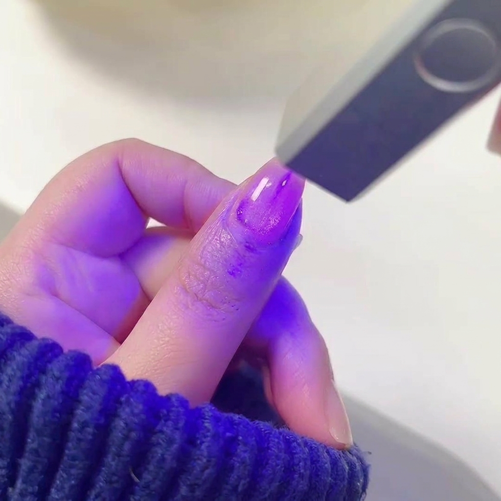 Un dito con smalto gel viola shimmer posizionato sotto la luce di una lampada UV/LED.