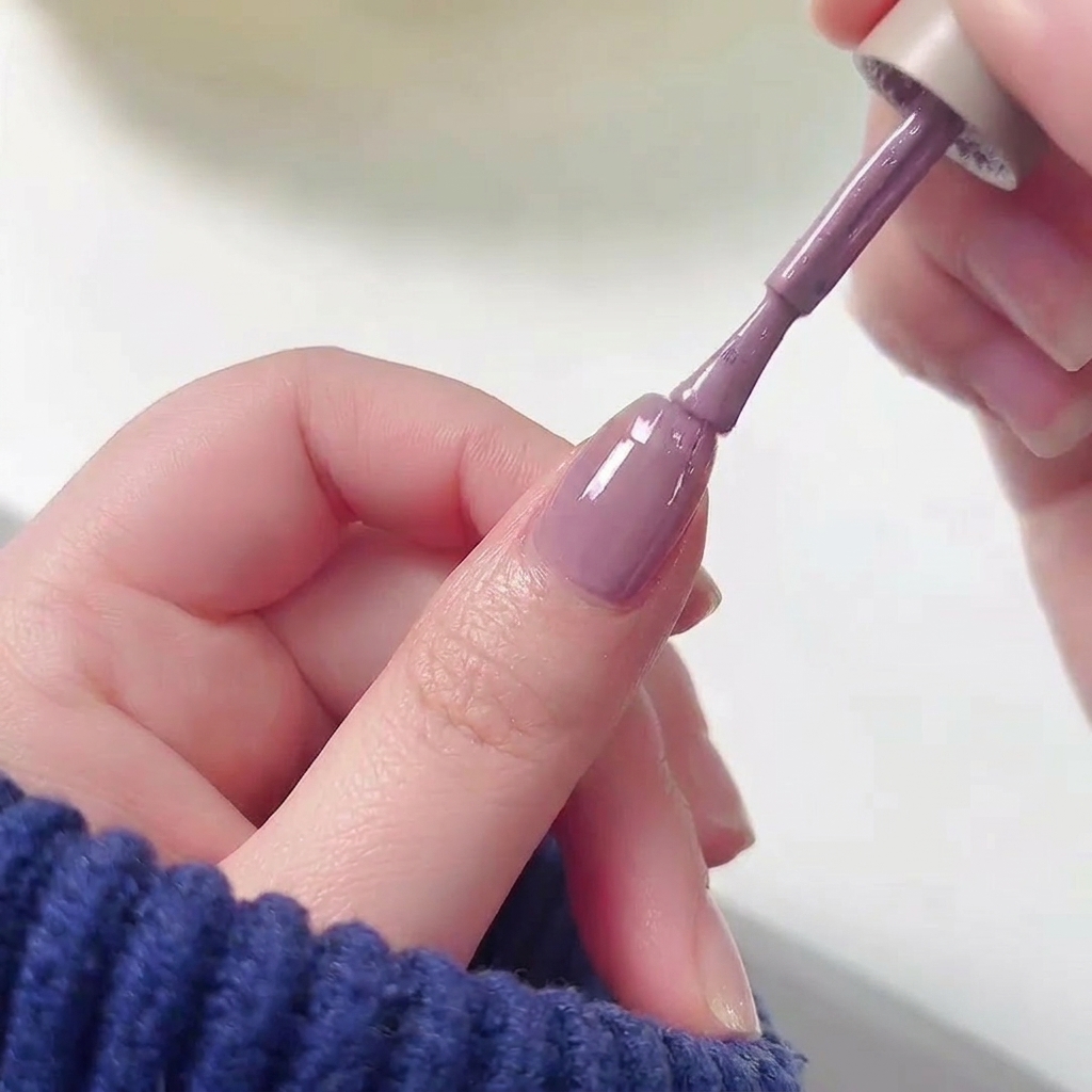 Pennello per smalto che applica il colore viola sulla metà superiore di ununghia già base rosa.