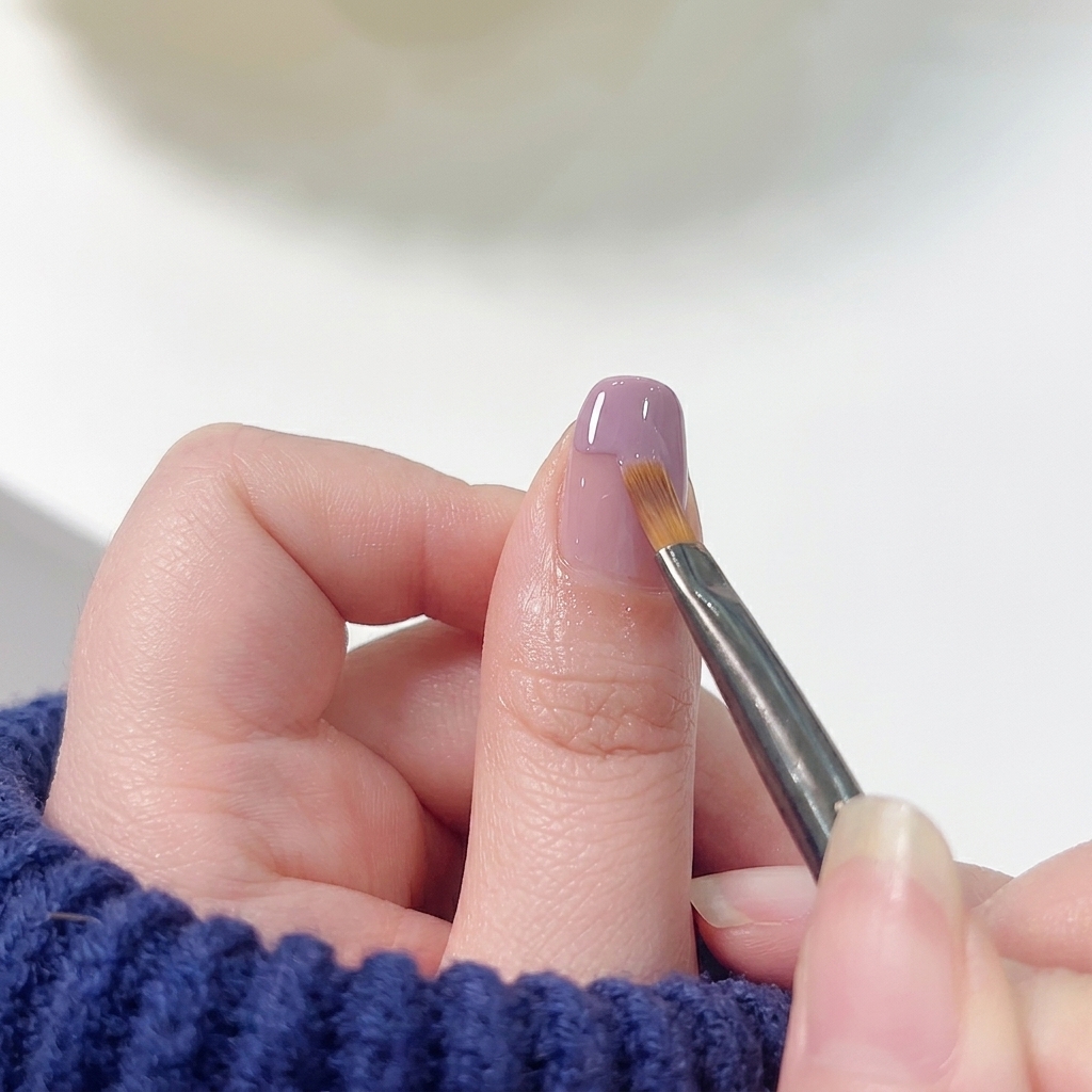 Un pennello piatto da nail art che trascina delicatamente il bordo dello smalto viola verso la base rosa.
