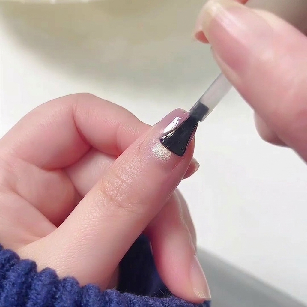 Pennello che applica un top coat lucido su ununghia con design sfumato rosa e viola.
