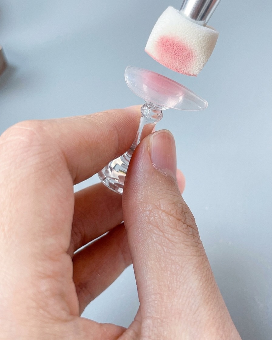 Primo piano di una spugnetta che applica un colore rosa confetto delicato su una tip da unghie su supporto.