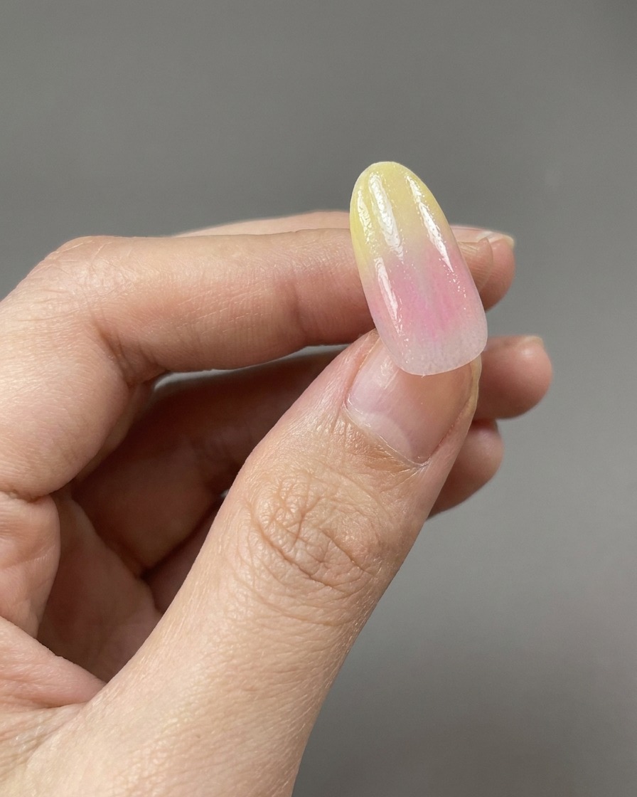 Un pennello che applica una base coat trasparente lucida su un design di unghie con gradiente giallo e rosa.