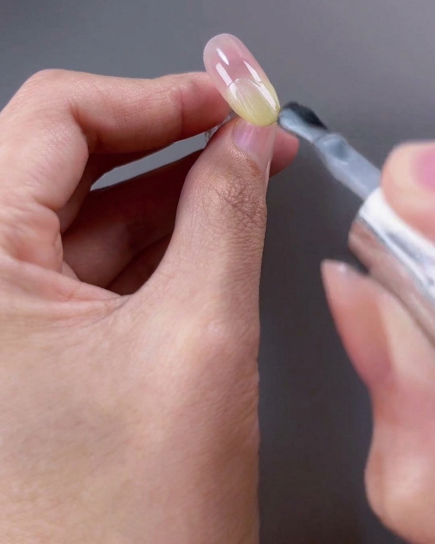 Un pennello da unghie che applica uno smalto gel cat-eye bianco traslucido sulla metà superiore dellunghia.