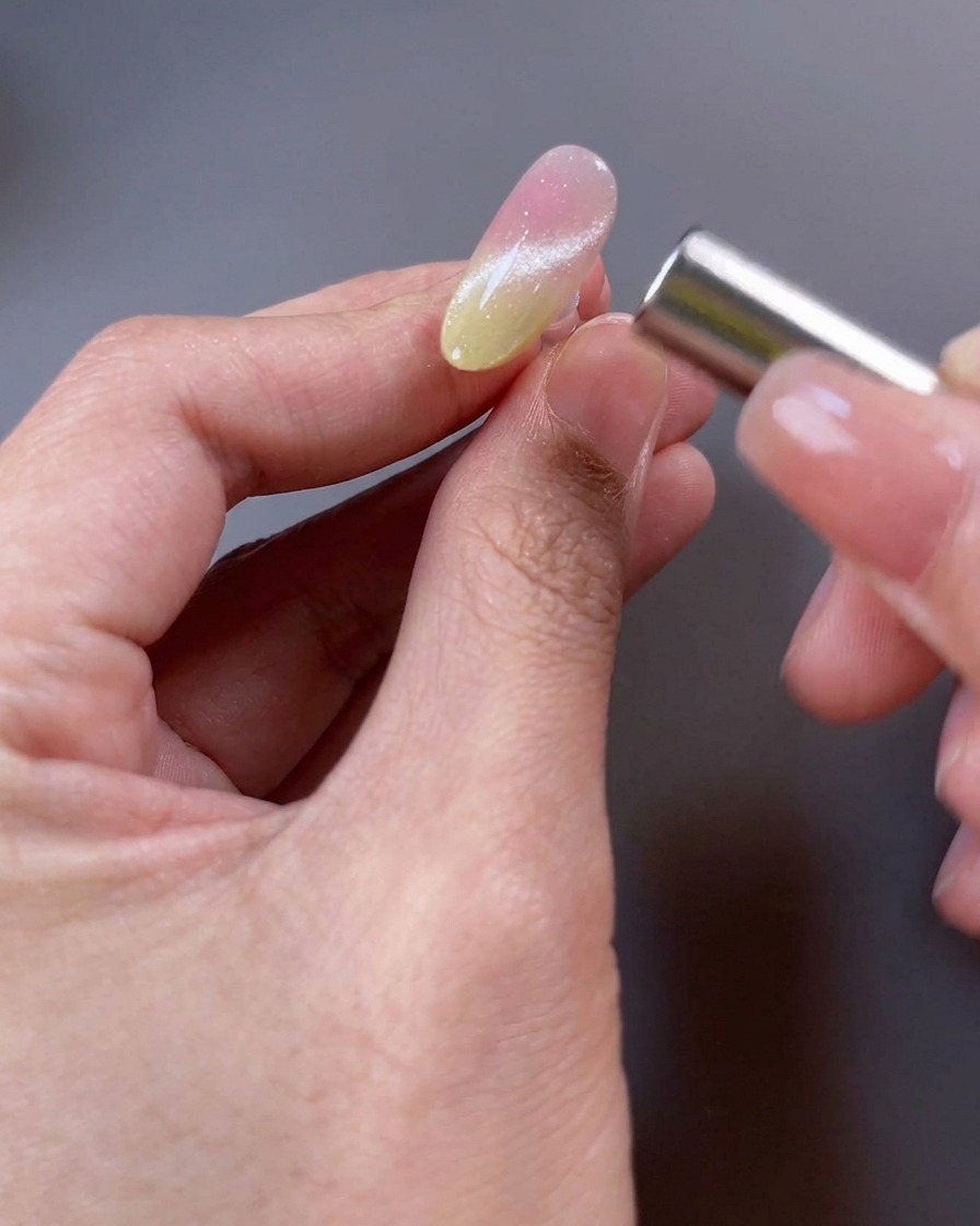 Primo piano di ununghia con smalto magnetico, con un magnete tenuto vicino alla superficie per manipolare le particelle in un fascio ampio.