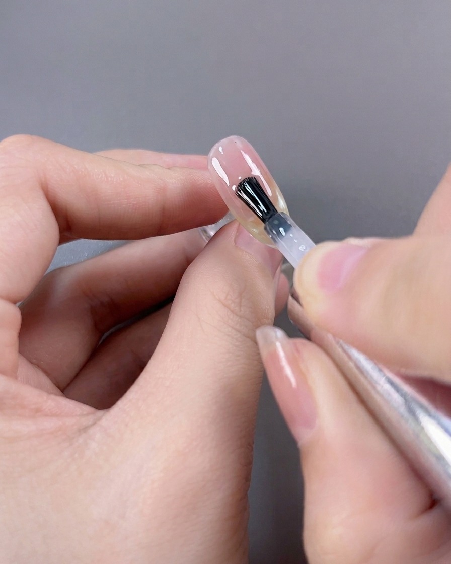 Un pennello che applica un top coat finale ultra-lucido su una manicure French cat-eye completata.