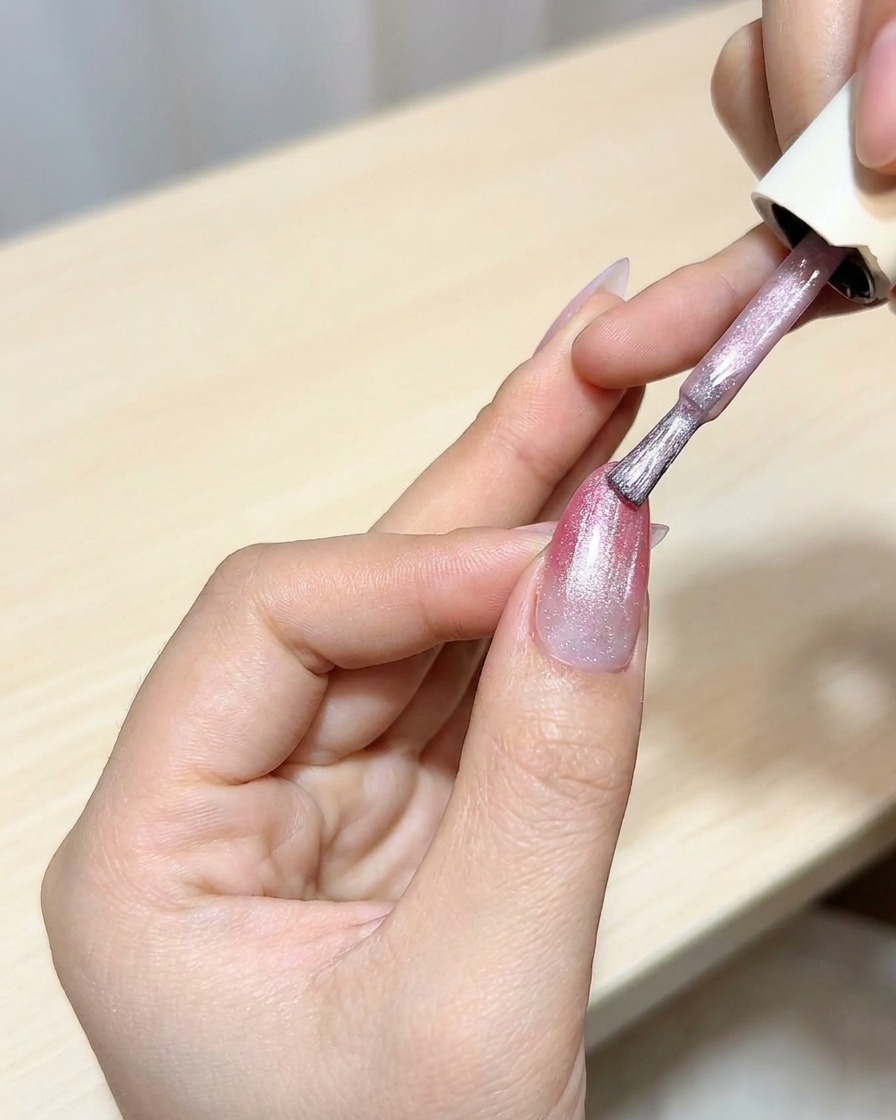 Un pennello applica uno strato di gel cat-eye sopra una base ombré magenta.