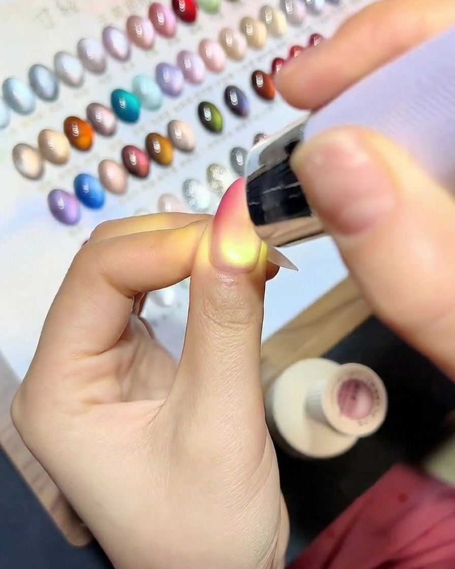 Un pennello applica un top coat trasparente e lucido sopra lunghia con effetto cat-eye sfumato.