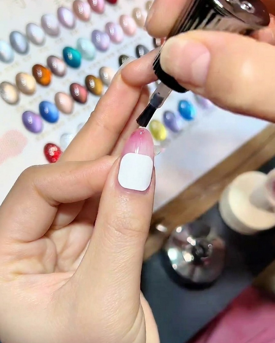 Primo piano di una mano con top coat appena applicato allinterno di una lampada professionale per unghie UV, illuminata da luce blu.