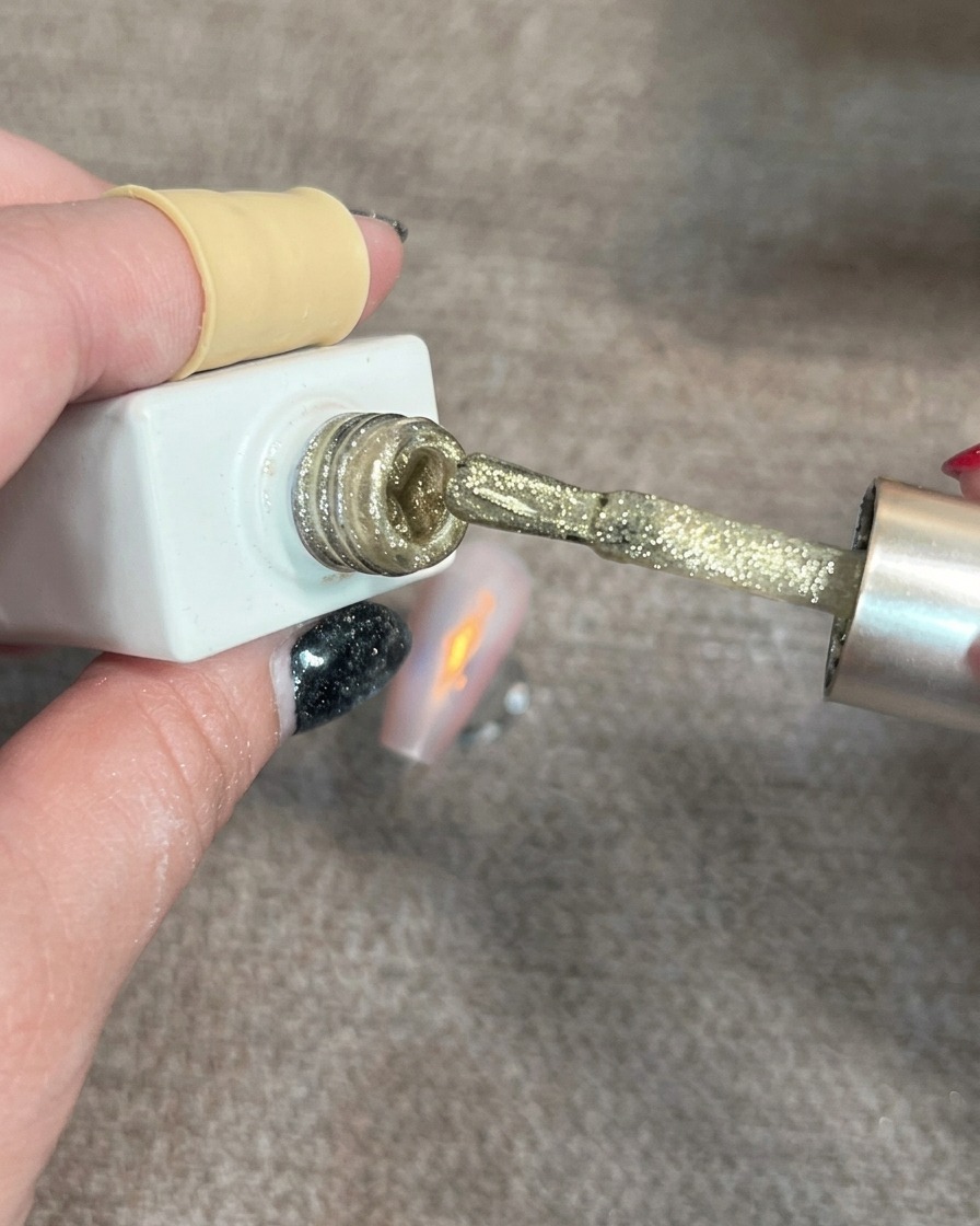 Un pennello che applica piccoli punti di gel cat-eye oro scintillante su ununghia parzialmente decorata.