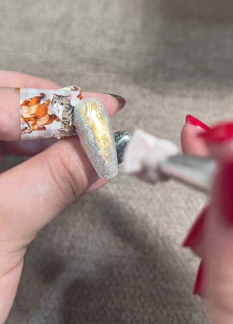 Un pennello da sfumatura che picchietta gel aranciato su ununghia multicolore per creare un gradiente morbido.