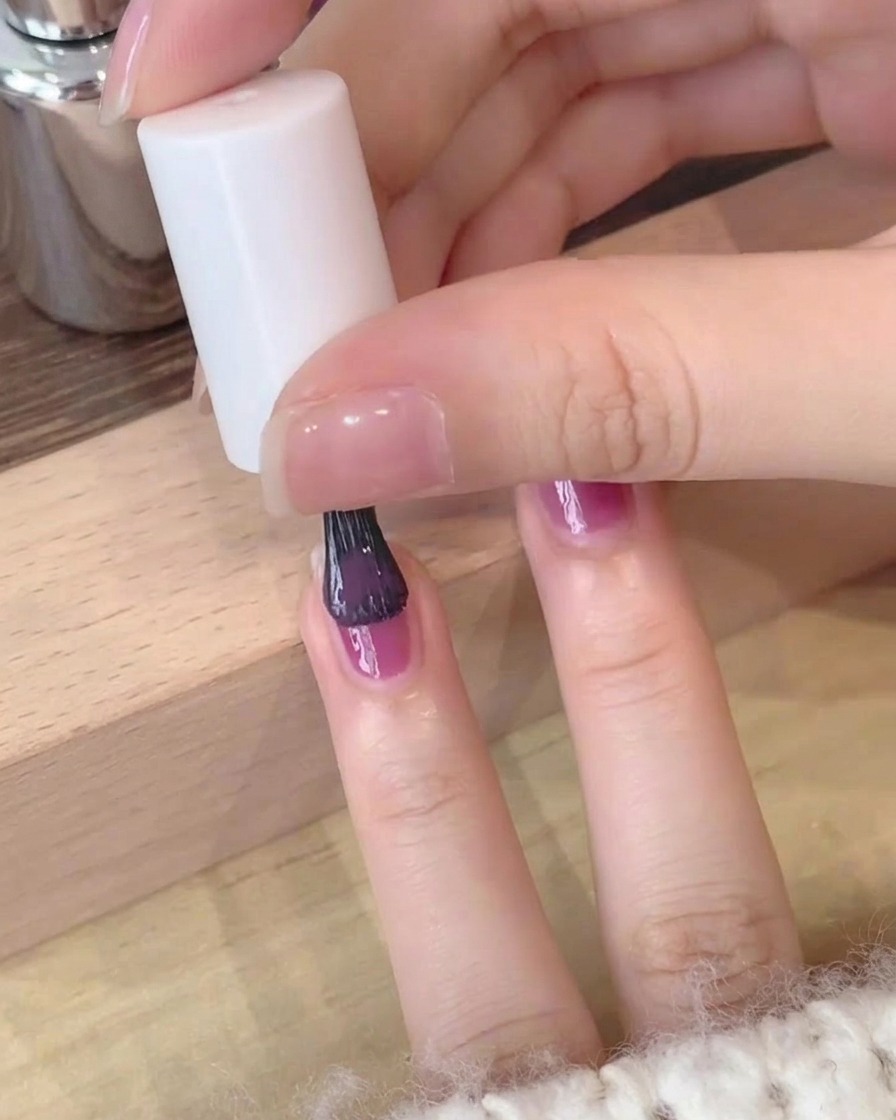 Primo piano di un secondo strato di smalto gel viola profondo applicato con cura su ununghia.