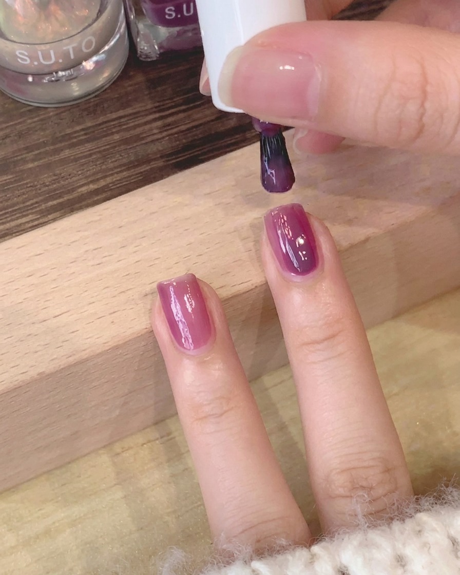 Un primo piano di un pennello che uniforma la superficie del gel viola sullunghia.