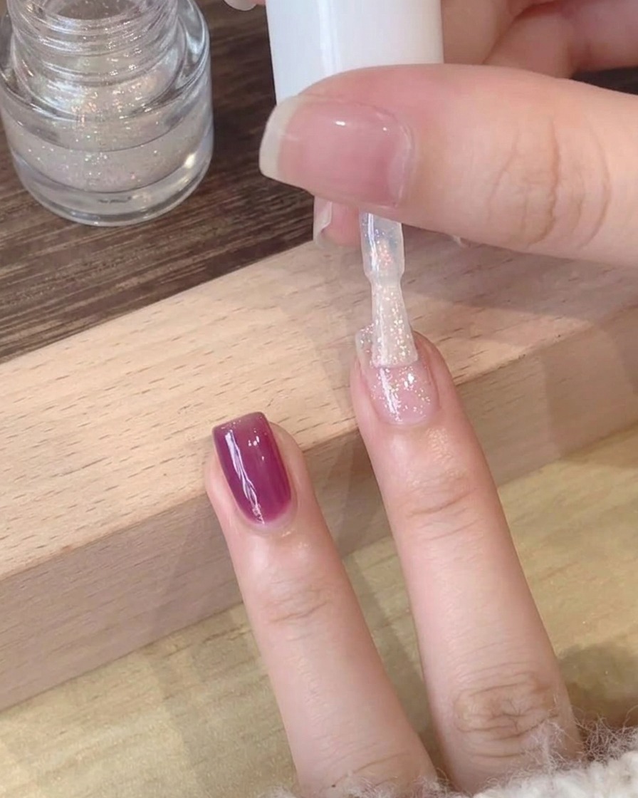 Un primo piano di un top coat scintillante polarizzato applicato sopra una base in gel viola profondo.