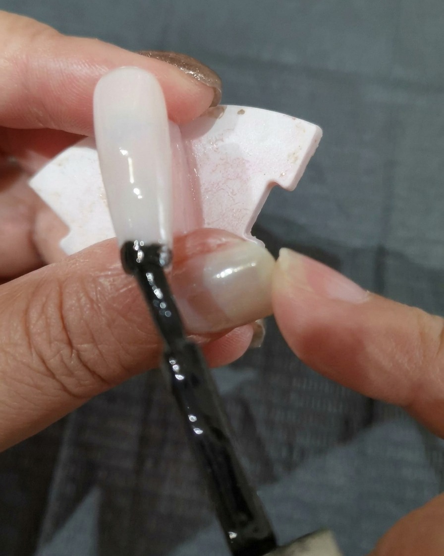 Un pennello applica uno strato di smalto gel nero su una tip.