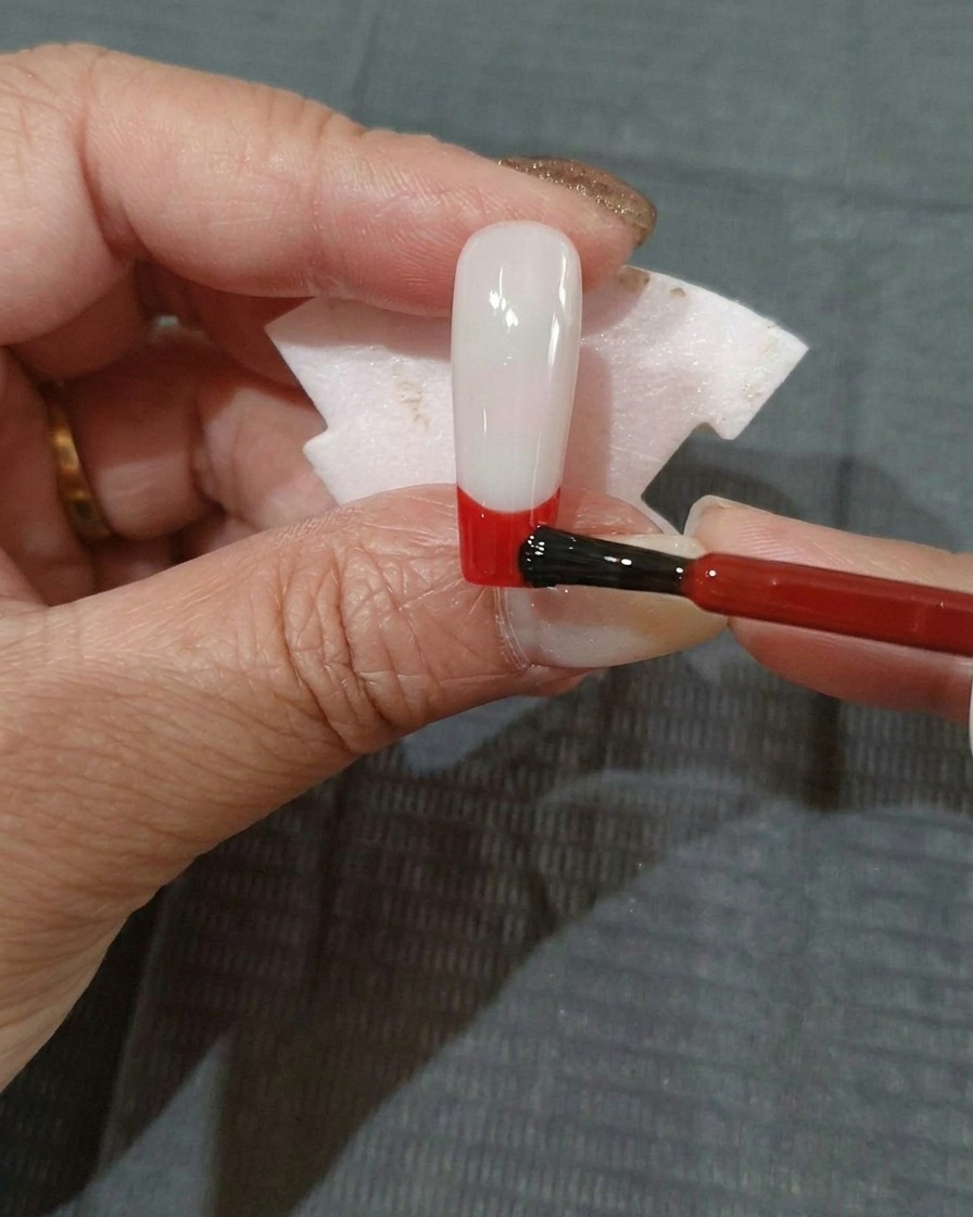 Uno strato sottile di smalto gel rosso applicato sulla parte inferiore di ununghia nera.