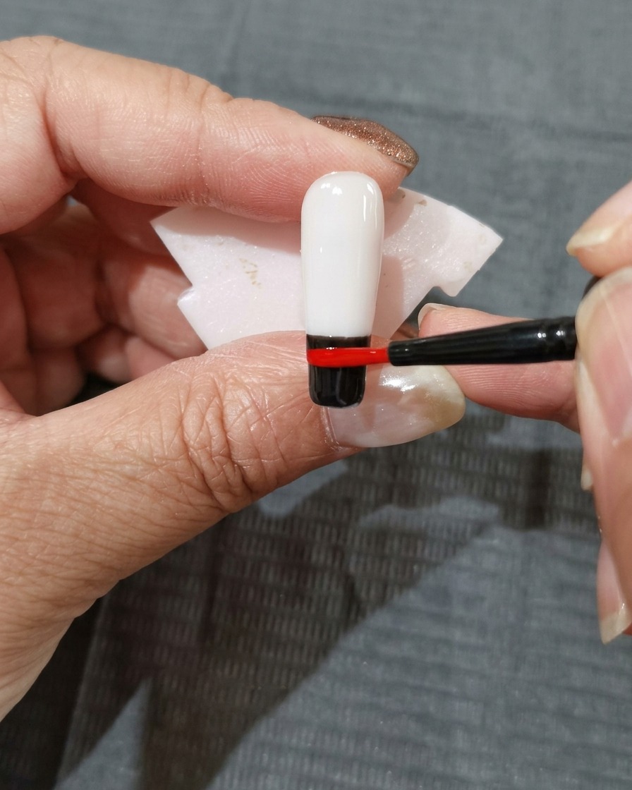 Una striscia di smalto gel rosso-arancio applicata sopra la fascia di colore rosso sullunghia.