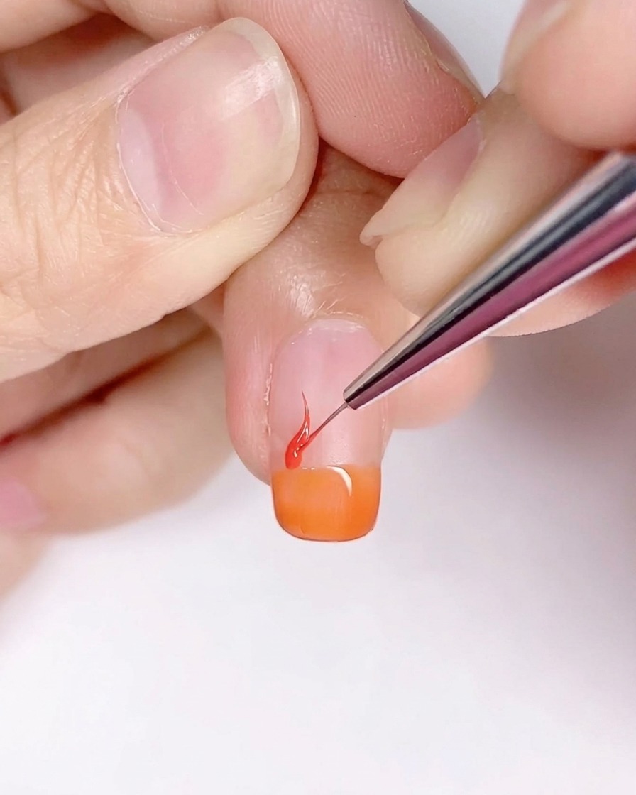 Un pennello a punta sottile crea forme a fiamma sullunghia con base arancione.