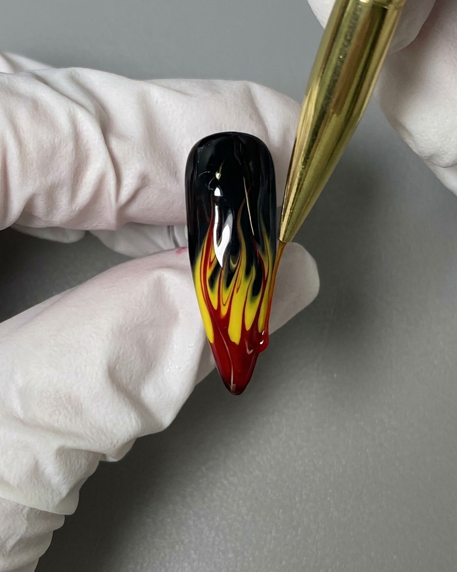 Un pennello liner applica un top coat lucido sopra la nail art con fiamme completata.
