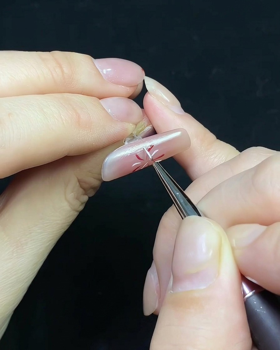 Un pennello che applica il top coat su ununghia decorata con fuochi dartificio e una piccola perla.
