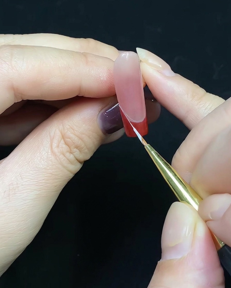 Un pennello a punta sottile che disegna una linea bianca lungo il bordo della french tip rossa.