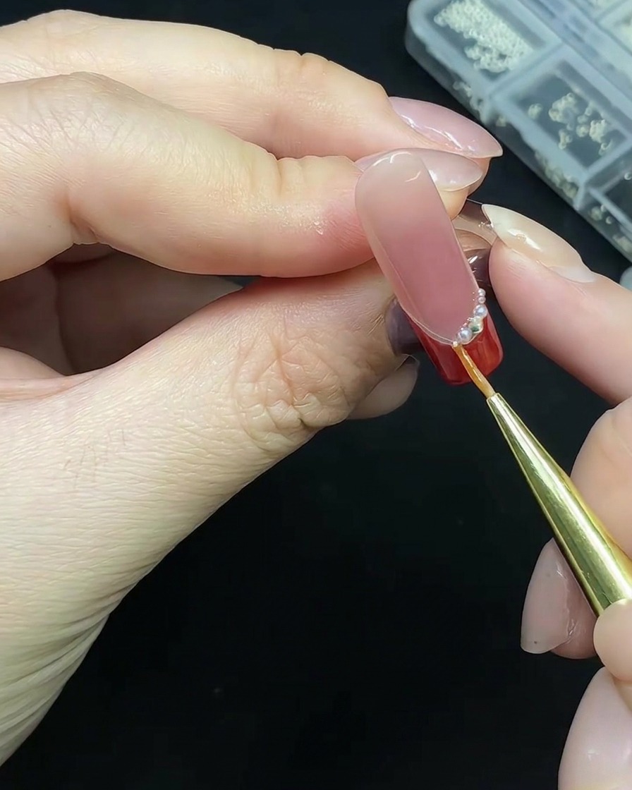 Uno strumento di precisione che posiziona piccole perle lungo la base della french tip rossa.