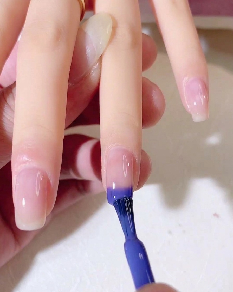 Un pennello per unghie applica uno smalto gel blu e viola sulla punta di ununghia naturale.