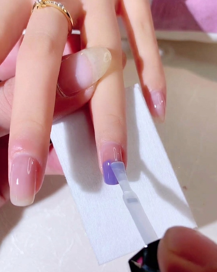 Un pennello per base coat in gel viene utilizzato per sfumare verticalmente i colori blu e viola su ununghia.