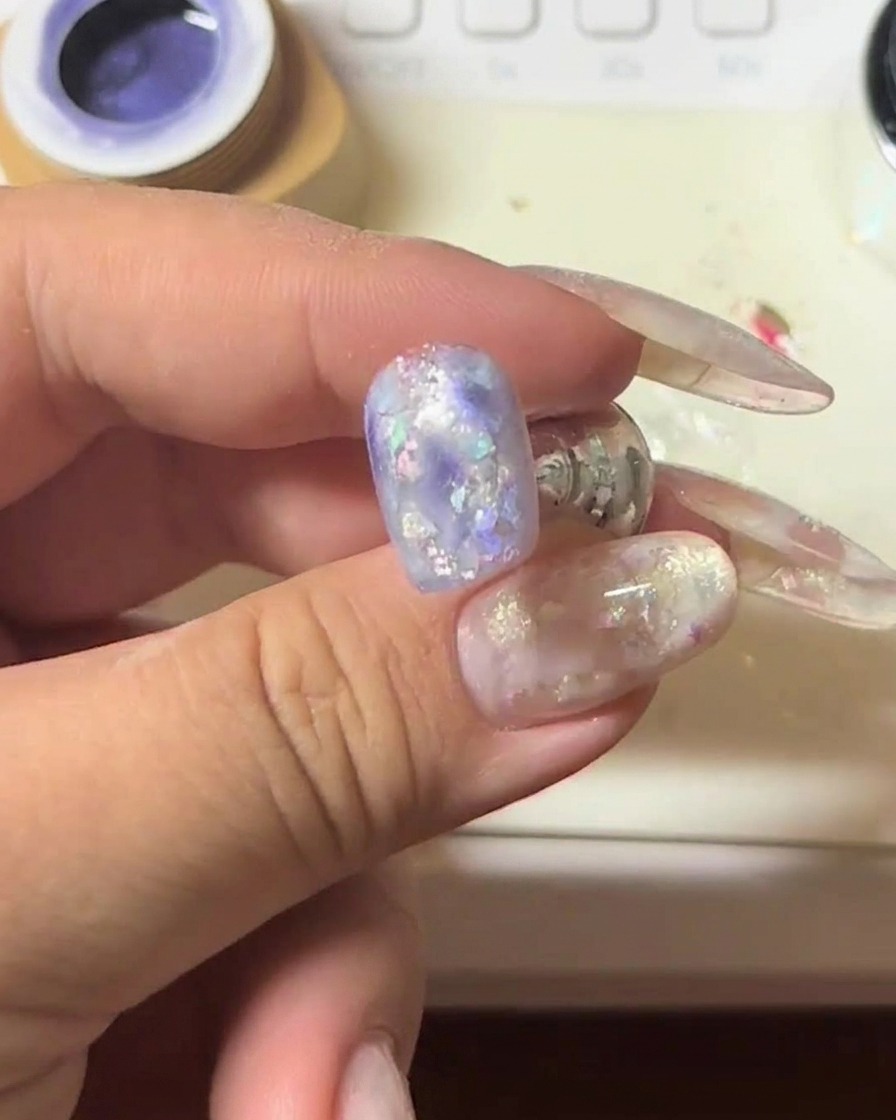 Primo piano di ununghia con gel cat-eye viola tenuta sotto un magnete per intensificare la striscia luminosa scintillante.