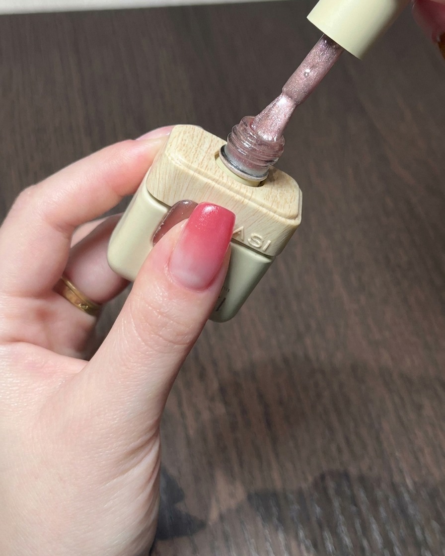 Un pennello applica un gel cat eye rosa nudo brillante sulla base sfumata rossa.