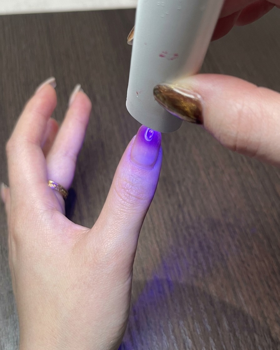 Una mano sotto una piccola lampada UV, che polimerizza il design finito dellunghia cat eye magnetica.