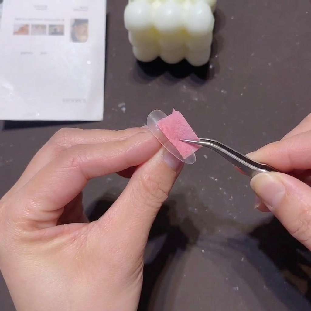 Una persona usa delle pinzette per tenere una piccola spugnetta rosa e tamponare un gel coprente chiaro sul bordo libero di una tip trasparente.