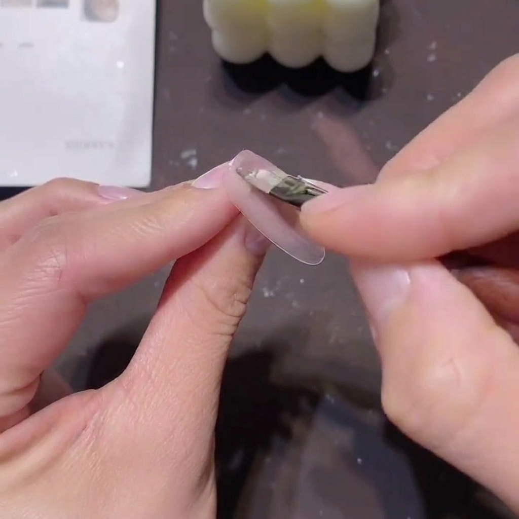 Un pennello applica un sottile strato di smalto gel rosa-nude traslucido su ununghia preparata.