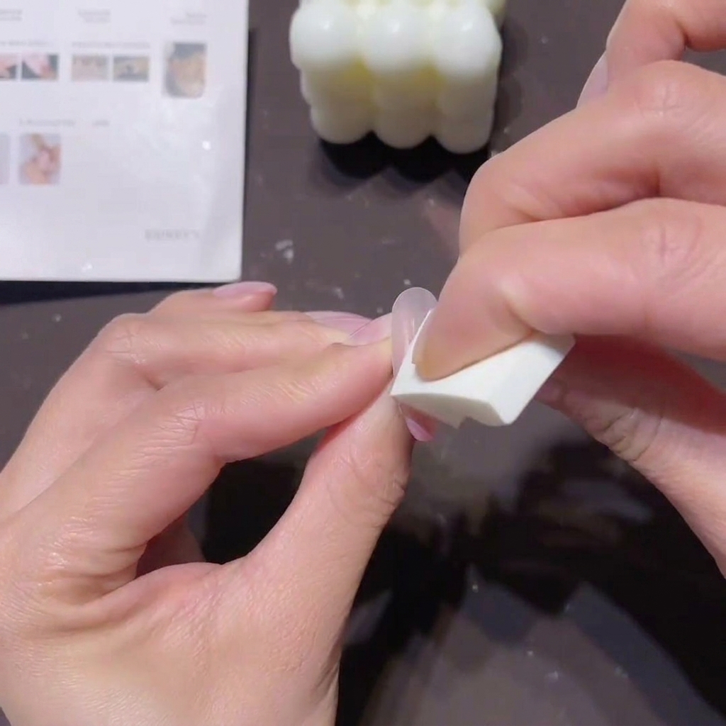Primo piano delle mani che usano una piccola spugnetta a cuneo per tamponare gel pesca-rosa sullunghia per creare un effetto ombré.