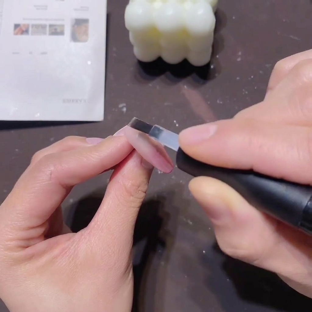 Un pennello piatto applica uno strato sottile di base coat trasparente sopra ununghia con sfumatura rosa per sigillare il colore.