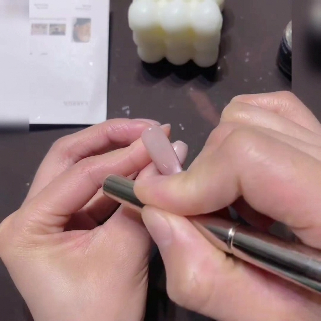 Una mano che tiene un magnete cilindrico, muovendolo con movimenti circolari attorno al bordo di ununghia rivestita di gel cat-eye.