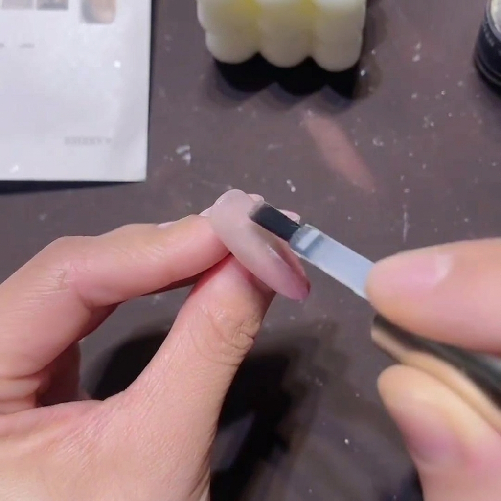 Un pennello piatto per gel applica uno strato spesso di top coat costruttore trasparente su un design unghie magnetico rosa finito.