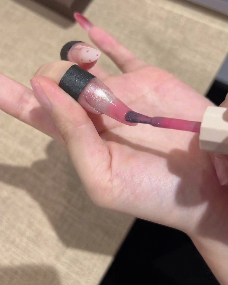 Un pennello di precisione che applica un gel rosa vibrante sulla punta di ununghia, sfumandolo per una finitura graduale.