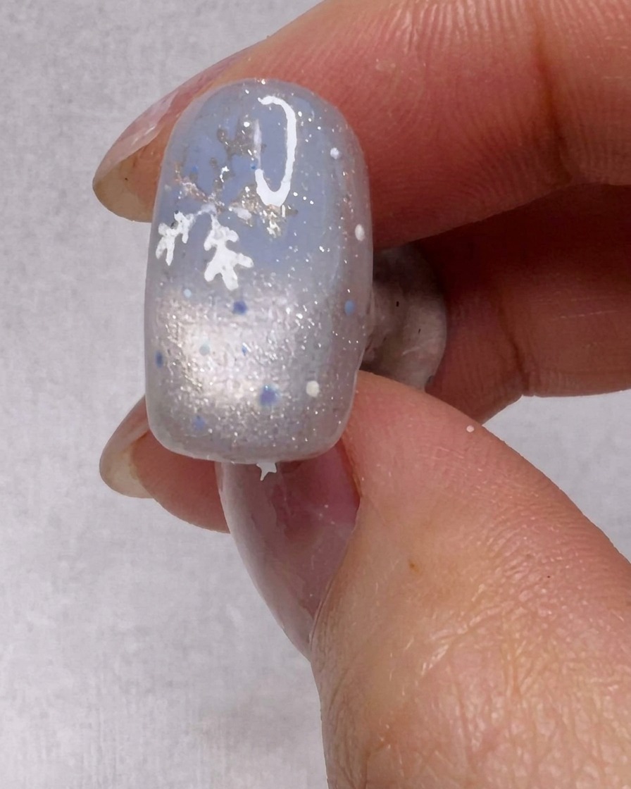 Un pennello che applica uno strato di smalto gel argentato scintillante su ununghia.